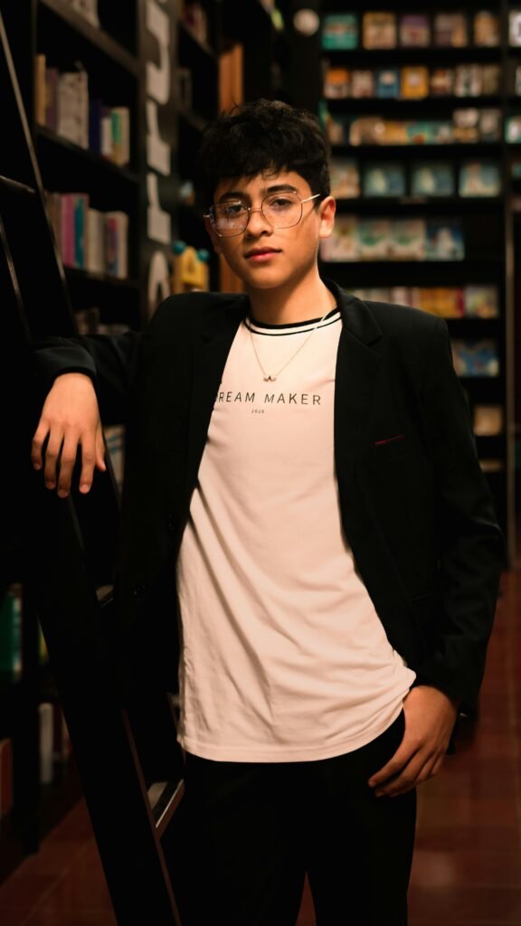 Fashionable young man with eyeglasses standing confidently in a library.