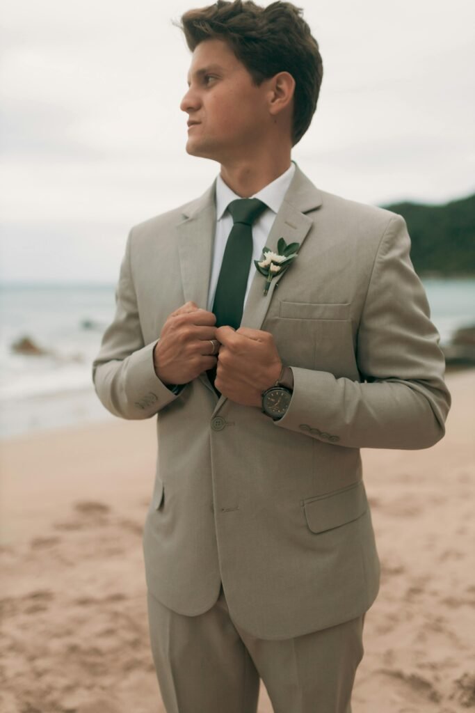 A man in a suit standing on a serene beach, looking confident and stylish against a beach backdrop.